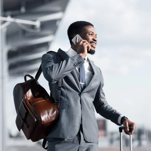 person dressed in a suit talks on phone while wheeling luggage