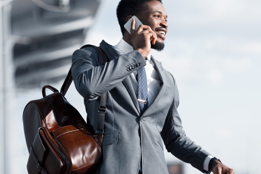 person dressed in a suit talks on phone while wheeling luggage